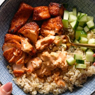 Air fryer salmon in a bowl with rice, cucumber, and sauce.