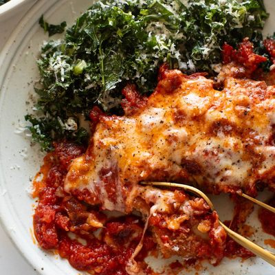 Chicken parmesan on a plate with kale salad.