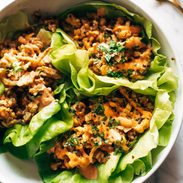 Lettuce wraps on a plate. The wraps are filled with tofu and brown rice and have sauce drizzled on top.