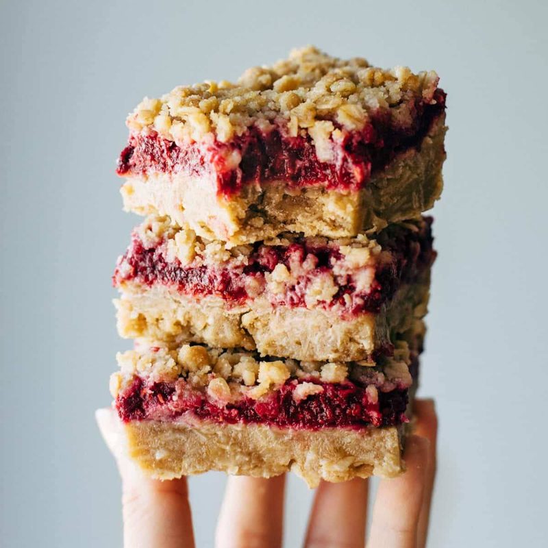Raspberry crumble bars stacked with a hand.